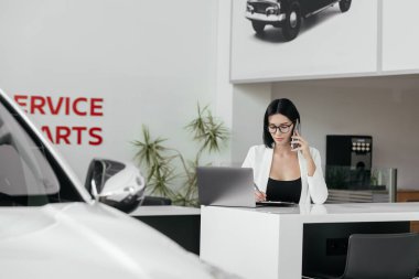 Güzel bayan yönetici belgelerle çalışıyor, telefonla konuşuyor ve modern ofiste dizüstü bilgisayar kullanıyor. servis ve parçalar          