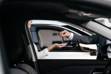 Modern bir araba galerisinde, alıcı ve satıcı anahtarları teslim ederek araba alımını tamamlar. Başarılı bir satın alma ve yeni bir araba sahibi olma kavramı.