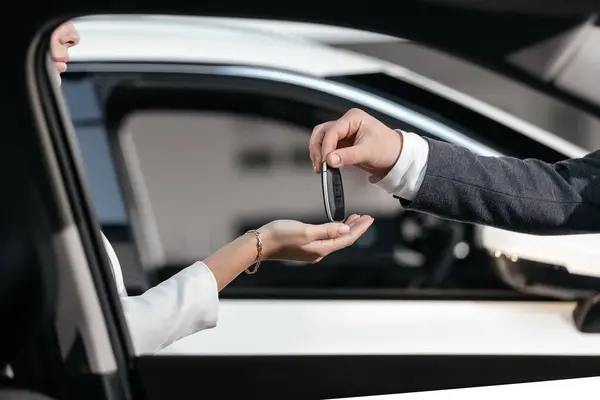 Modern bir araba galerisinde, alıcı ve satıcı anahtarları teslim ederek araba alımını tamamlar. Başarılı bir satın alma ve yeni bir araba sahibi olma kavramı.