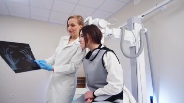 Beyaz önlüklü doktor kadın hastanın röntgenini inceliyor.