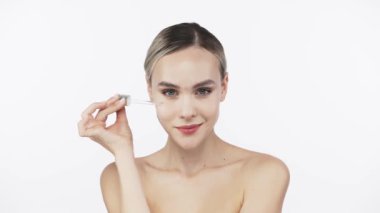 Kadın beyaz arka planda pipetle nemlendirici sıvı uyguluyor.