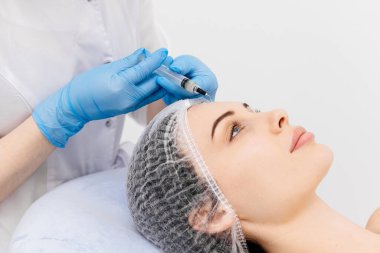Genç bir kadına yüz bakımı yapan bir kozmetikçinin yakın çekimi. Profesyonel bakım, gençleştirme ve sağlıklı cilt kavramı.
