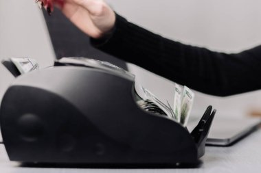 Bilgisayarın yanında para sayma makinesi olan tanınmayan bir kadın para bozdurmak ya da para yatırmak için yüz dolarlık banknotları sıralıyor. Finansal konsept, kredi veya volt değişimi.