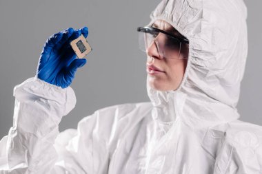 Steril tulumlu bir kadın mühendisin, ileri teknoloji ve hassas mühendislik ürünleri sergilemek için mükemmel bir teknoloji fabrikasında eldivenli elleri olan bir mikroçipi incelemesi..