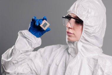 Steril tulumlu bir kadın mühendisin, ileri teknoloji ve hassas mühendislik ürünleri sergilemek için mükemmel bir teknoloji fabrikasında eldivenli elleri olan bir mikroçipi incelemesi..