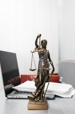 Bir avukatın çalışma alanına dizüstü bilgisayar ve Themis 'in heykeliyle yakın çekim. Hukuk dünyasında hukuk, adalet ve profesyonelliğin sembolü..