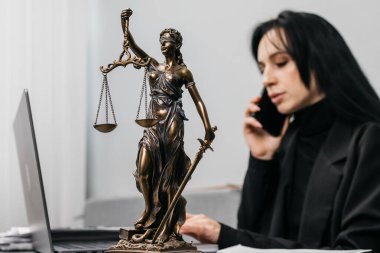 Modern bir ofiste çalışan genç bir bayan avukat, telefonda bir müşteriye danışıyor. Themis 'in heykeli yakınlarda, adalet, yargı ve hukuk kavramı.