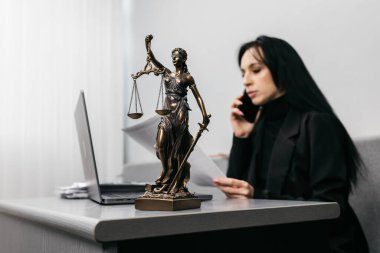 Modern bir ofiste çalışan genç bir bayan avukat, telefonda bir müşteriye danışıyor. Themis 'in heykeli yakınlarda, adalet, yargı ve hukuk kavramı.