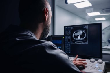 Erkek doktor bilgisayar ekranına bakarken hastanın MRI taramasını inceliyor.