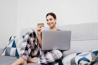 Kredi kartı tutan ve evinde dizüstü bilgisayar kullanan bir kadın. çevrimiçi alışveriş kavramı