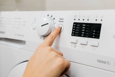 Kadın elinin çamaşır makinesinin düğmelerine dokunuşu.
