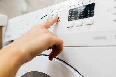 Kadın elinin çamaşır makinesinin düğmelerine dokunuşu.