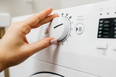 Kadın elinin çamaşır makinesinin düğmelerine dokunuşu.