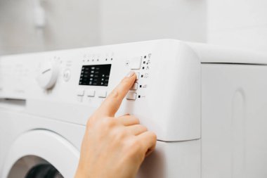 Kadın elinin çamaşır makinesinin düğmelerine dokunuşu.