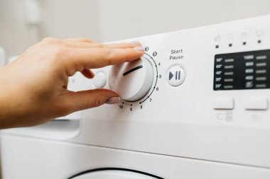 Kadın elinin çamaşır makinesinin düğmelerine dokunuşu.