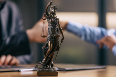 Masanın üzerindeki tanrıça heykeli insanların bulanık arka plan, hukuk ve adalet kavramında el sıkışması..