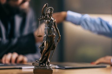 Masanın üzerindeki tanrıça heykeli insanların bulanık arka plan, hukuk ve adalet kavramında el sıkışması..