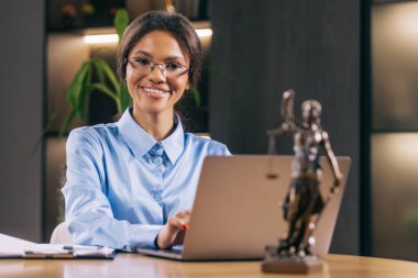 Dizüstü bilgisayarla çalışan gülümseyen genç avukat kadın ve masadaki tanrıça heykeli.