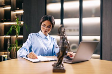 Dizüstü bilgisayarla çalışan konsantre genç avukat kadın ve masadaki tanrıça heykeli, seçici odaklanma