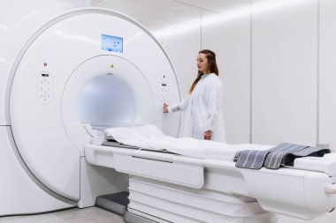 Genç bayan doktor hastanede MRI tarama makinesini kontrol ediyor.