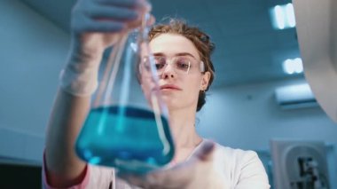 Koruyucu eldiven ve gözlüklü bilim adamı laboratuarda sıvı içeren test tüpüne bakıyor.