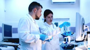 Mavi eldiven giyen bir bilim adamı mavi bir sıvıyı analiz eder. Kimyasallar ve modern araştırma yöntemleriyle yapılan kesin bilimsel deneyler konsepti.