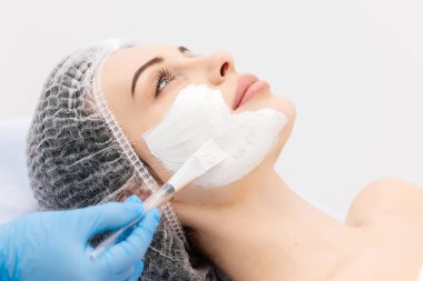 Profesyonel bir güzellik salonunda cilt bakımı sırasında genç bir kadının yakın çekimi. Kozmetik uzmanı kilden bir maske takıyor. Kozmetik, cilt bakımı ve cilt tazeleme kavramı.