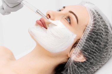 Profesyonel bir güzellik salonunda cilt bakımı sırasında genç bir kadının yakın çekimi. Kozmetik uzmanı kilden bir maske takıyor. Kozmetik, cilt bakımı ve cilt tazeleme kavramı.