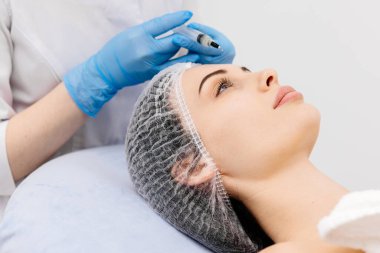 Bir kozmetolog, profesyonel bir güzellik salonunda genç bir kadının yüzüne kimyasal kabuk bağlıyor. Etkili cilt bakımı, gençleştirme ve cilt yenileme kavramı.