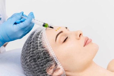 Bir kozmetolog, profesyonel bir güzellik salonunda genç bir kadının yüzüne kimyasal kabuk bağlıyor. Etkili cilt bakımı, gençleştirme ve cilt yenileme kavramı.