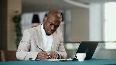 Modern bir ofiste masa başında çalışan, telefonla konuşan ve bir dizüstü bilgisayar üzerinde çalışan odaklanmış Afro-Amerikalı bir adam. Sıkı çalışma, yorgunluk ve profesyonellik kavramı.