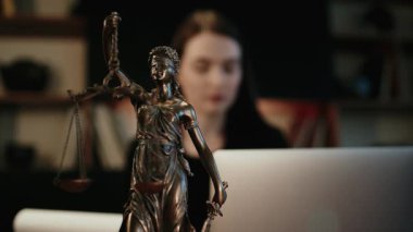 Avukatın masasında bir Adalet Heykeli ve sıcak ışık altında bir dizüstü bilgisayar. Adalet, profesyonellik ve hukuki uzmanlık kavramı.