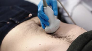 Klinikteki bir adam için karın organlarının ultrason teşhisi. Doktor hastanın karnındaki ultrason sondasını hareket ettiriyor. Doğru tanı koymak için gelişmiş tıbbi teknoloji kavramı.