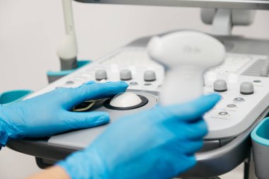 Kadın elleri koruyucu eldivenlerle klinikte ultrasonla çalışıyor.