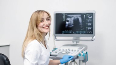 Portrait of a young female ultrasound specialist near a screen displaying scan results. The concept of modern technology and a professional approach in medical imaging. clipart