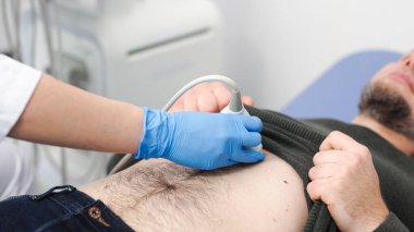 Klinikteki bir adam için karın organlarının ultrason teşhisi. Doktor hastanın karnındaki ultrason sondasını hareket ettiriyor. Doğru tanı koymak için gelişmiş tıbbi teknoloji kavramı.