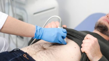 Klinikteki bir adam için karın organlarının ultrason teşhisi. Doktor hastanın karnındaki ultrason sondasını hareket ettiriyor. Doğru tanı koymak için gelişmiş tıbbi teknoloji kavramı.