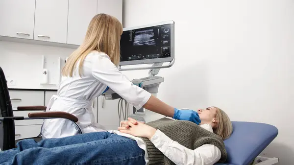 Tiroit ultrasonuna yakın çekim. Mavi eldivenli bir doktor genç bir hastanın boynundaki sondayı hareket ettiriyor. Modern teknoloji ve endokrin tanı konularında hassasiyet kavramı.