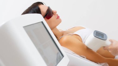 Kadın klinikte lazer tedavisi görüyor, koltuk altındaki kılları alıyor.