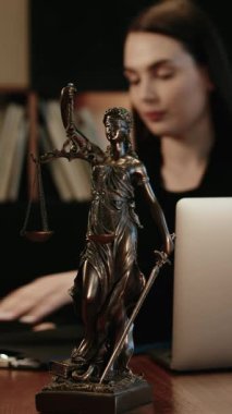 Dikey video. Avukatlık bürosu. Terazili adalet heykeli ve dizüstü bilgisayarda çalışan bir avukat. Hukuk kavramı, hukuki danışmanlık ve adalet.