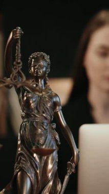 Dikey video. Avukatlık bürosu. Terazili adalet heykeli ve dizüstü bilgisayarda çalışan bir avukat. Hukuk kavramı, hukuki danışmanlık ve adalet.
