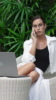 Kendine güvenen bir iş kadını tropik bir ortamda dizüstü bilgisayarda çalışıyor. Başarılı bir kariyer, esneklik ve dünyanın her yerinden çalışma kavramı..