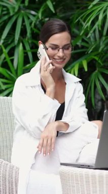 Bilgisayarla çalışırken telefonla konuşan modern bir iş kadını. Modern bir ofiste profesyonel bir yönetici iş görüşmesi yapıyor. İş kavramı, çoklu görev ve verimli iş akışı.