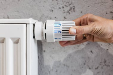  Radyatörün sıcaklığını ayarlayan bir el. Enerji tasarrufu, ısıtma sistemleri ve ev konforunu vurgulayan bir kavram. Enerji tasarruflu yaşam ve kışlık ev çözümleri için ideal.