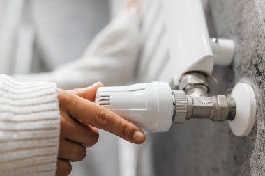 Radyatörün sıcaklığını ayarlayan bir elin yakın çekimi. Enerji tasarrufu, ısıtma sistemleri ve ev konforunu vurgulayan bir kavram.