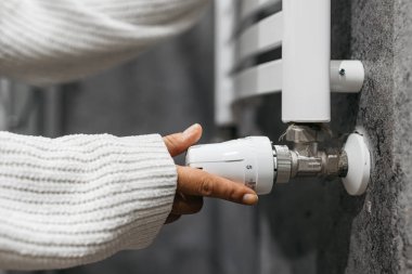 Radyatörün sıcaklığını ayarlayan bir elin yakın çekimi. Enerji tasarrufu, ısıtma sistemleri ve ev konforunu vurgulayan bir kavram.