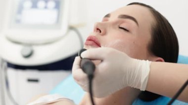 Bir kozmetikçi modern bir klinikte genç bir bayana radyasyon tedavisi uygular. Cilt sıkılaştırma ve gençleştirme için gelişmiş prosedürler kavramı güzellik gösterileri için mükemmeldir..