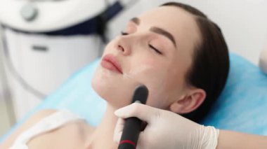 Bir kozmetikçi modern bir klinikte genç bir bayana radyasyon tedavisi uygular. Cilt sıkılaştırma ve gençleştirme için gelişmiş prosedürler kavramı güzellik gösterileri için mükemmeldir..