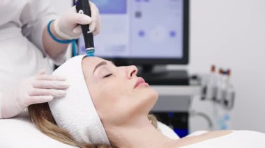 Bir profesyonel, modern bir kuaförde genç bir kadının cildini temizleyip canlandırmak için hidrojen soyarak yüz bakımı yapar. Cilt geliştirme için yenilikçi teknolojiler kullanma kavramı.