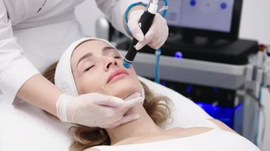 Bir profesyonel, modern bir kuaförde genç bir kadının cildini temizleyip canlandırmak için hidrojen soyarak yüz bakımı yapar. Cilt geliştirme için yenilikçi teknolojiler kullanma kavramı.